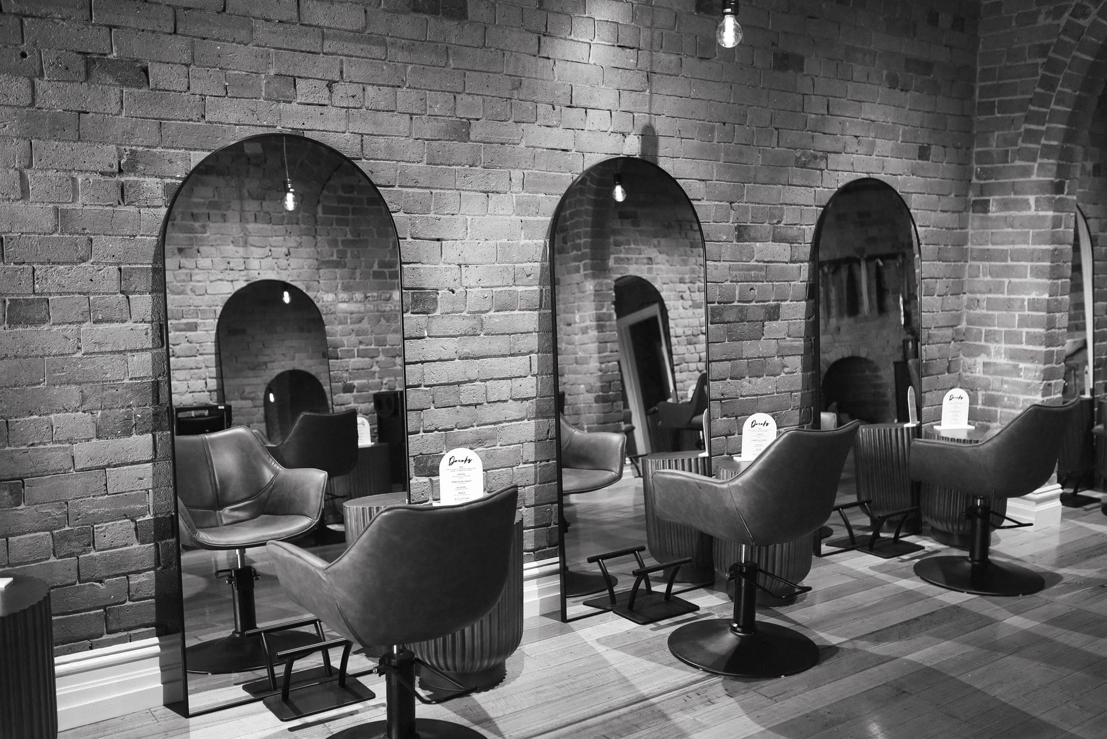 Black and white view of Hair and Halo Studio styling stations with arched mirrors and exposed brick